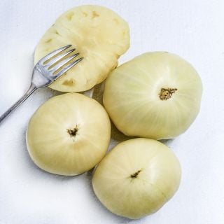 Three whole and a halved Great White Tomatoes with a vintage silver fork on a white background.