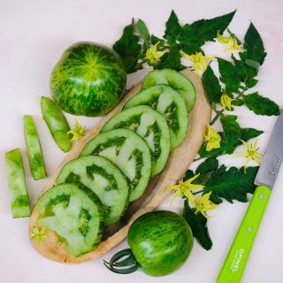 Green Zebra Tomatoes sliced on a wood serving dish surrounded by leaves and blooms.