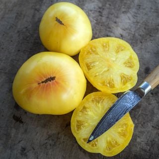 Whole and sliced Hugh's Tomatoes on a wood cutting board with a knife.