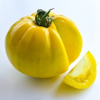 A single bright yellow Hugh's Tomato with a slice cut out of it on a white background.