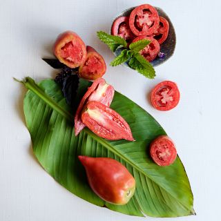 Sliced and whole Korean Long Tomatoes on a large leaf on a linen background.