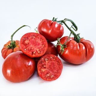 A half dozen whole and halved Pantano Romanesco Tomatoes arranged on white background.