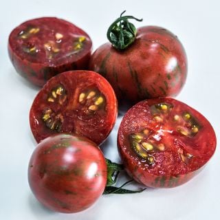 A close-up macro view of cut and whole Purple Bumble Bee Tomatoes on a white background.