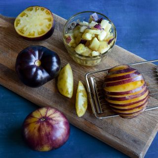 Sliced, cut and whole Sart Roloise Tomatoes on a cutting board against a deep blue background.