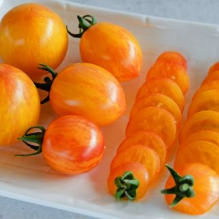 Whole and sliced Sunrise Bumble Bee Tomatoes on a white plate.