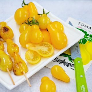 Roasted and fresh Yellow Pear Tomatoes on a white plate with a vintage seed packet and knife.