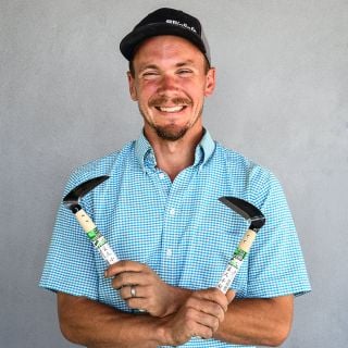 The Baker Creek garden manager smiles as he holds a Left and Right Handed Professional Sickle in each hand.