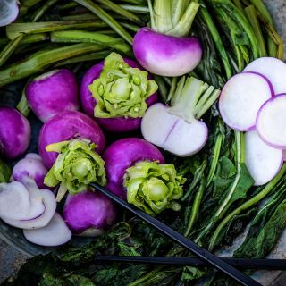 Close-up view of sauteed greens with Nagasaki Akari Kabu turnips in ceramic bowl.