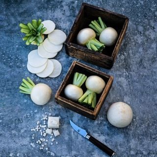 Two wooden boxes holding Tokinashi Turnips with a sliced turnip beside them on a grey background.