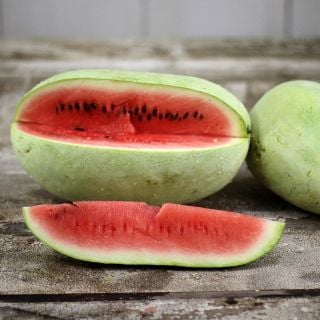 Ali Baba Watermelon with a slice cut on a weathered wooden background.