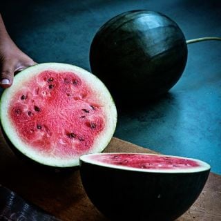 Woman cutting a Blacktail Mountain Watermelon on cutting board with a whole melon in the background.