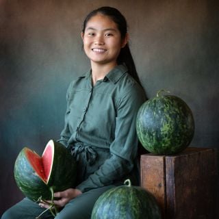 Smiling young woman holding a cut Wilson's Sweet Watermelon with a couple of whole melons.