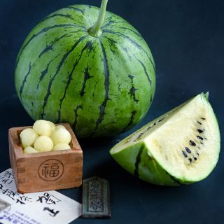 A whole Silver Yamato Watermelon with a quarter slice and melon balls in a wooden Japanese box on a jade background.