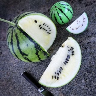 A cut Silver Yamato Watermelon with a Japanese knife and watermelon shaped salt shakers on stone.