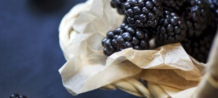 Dark blue background with a pale wicker basket containing fresh boysenberries on a pale beige napkin or towel