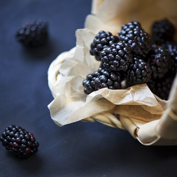 fresh boysenberries in a basket lined with a light colored napkin on a dark blue background